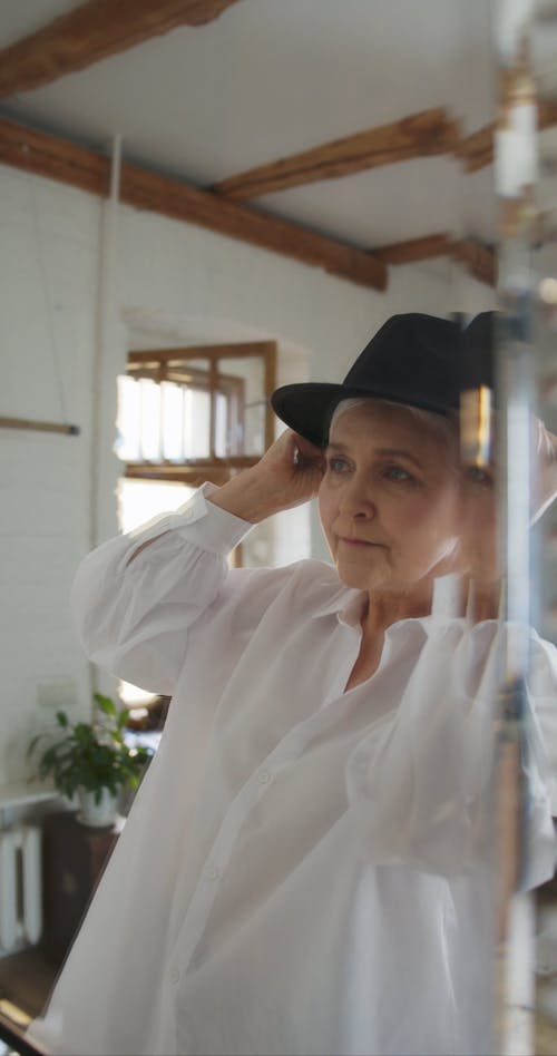 An Elderly Woman Trying On A Hat In Front Of A Mirror