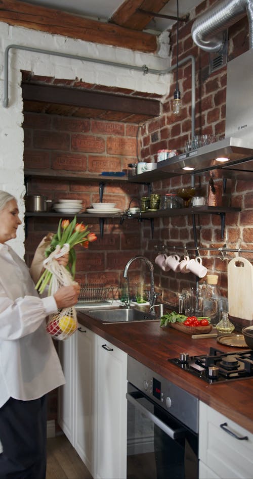 An Elderly Woman Setting Up A Bunch Tulips Flower On A Jug Of Water