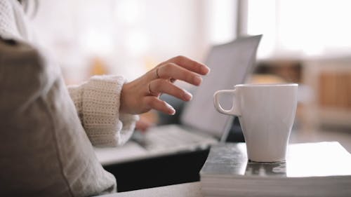 A Woman Drinking Coffee while Typing on her Laptop