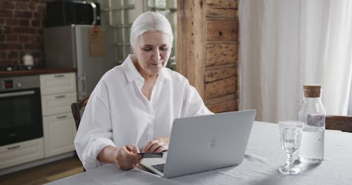 An Elderly Woman Using A Bank Card And A Laptop For Transaction