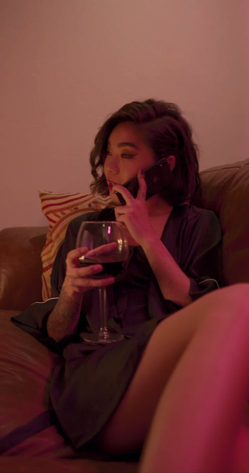 A Woman Holding A Glass Of Wine While Talking On Her Phone