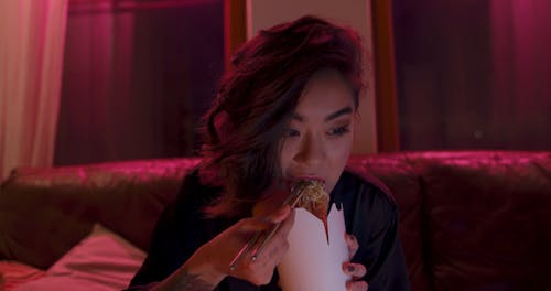 A Woman Eating Take Home Noodles Using Chopsticks