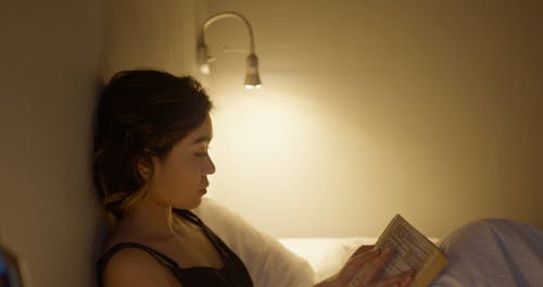 A Woman Turning Off The Light After Reading In Bed To Sleep