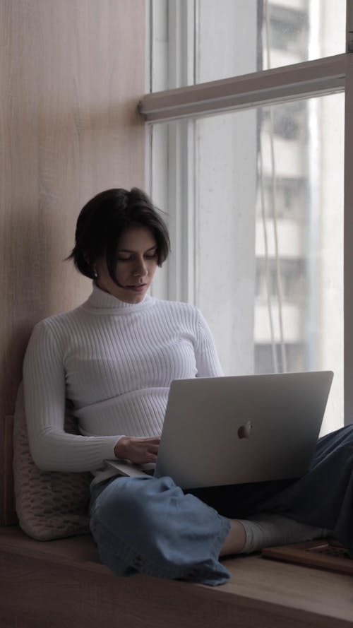 A Woman Sitting Beside the Window while Using her Laptop
