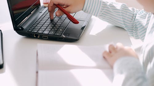 A Boy Using A Laptop And Taking Notes