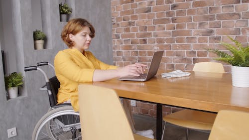 A Woman In a Wheelchair Typing On A Laptop Keyboard