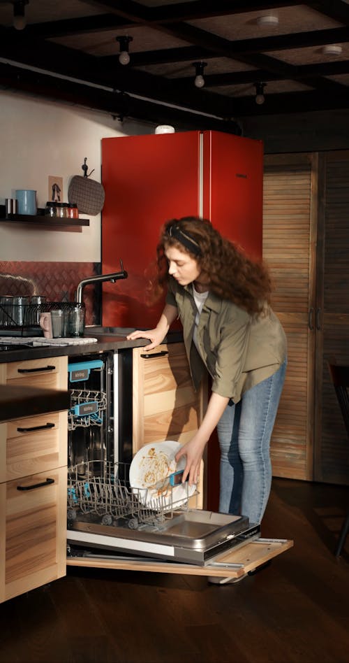 A Woman Placing The Dirty Dishes Inside The Automatic Dish Washer