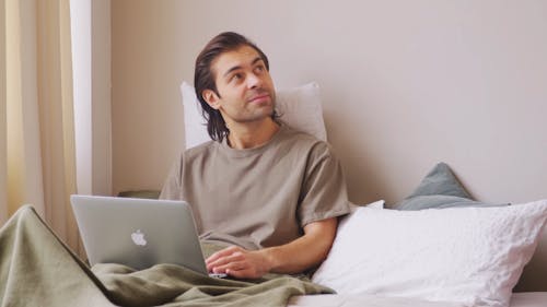 Couple Sitting Down the Bed while Using the Laptop