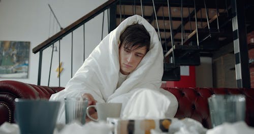 A Sick Man Cover Himself With A Thick Blanket While Drinking Hot Tea