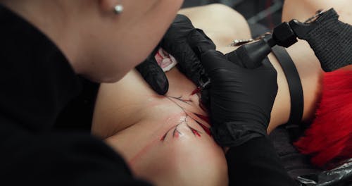 A Tattoo Artist Drawing A Flower With Red Ink On A Customer Shoulder