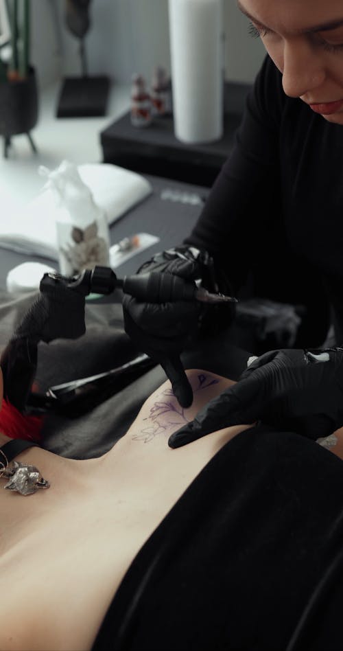 A Female Tattoo Artist Tattooing A Woman's Shoulder