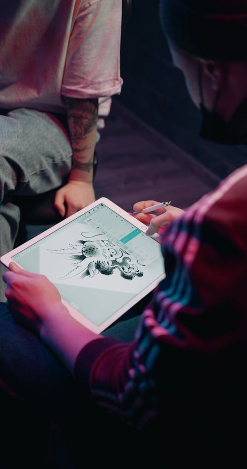 A Tattoo Artist Using An Ipad To Show A Customer A Dragon Design