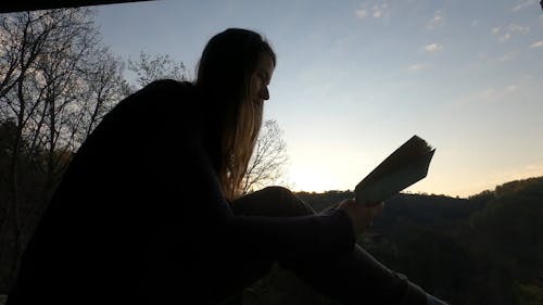 A Woman Reading a Book while Enjoying the Sunrise