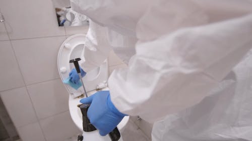 Person in Coveralls Disinfecting Toilet