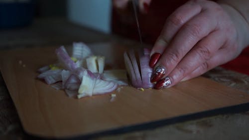 Cutting An Onion With A Knife Over A Wooden Chopping Board