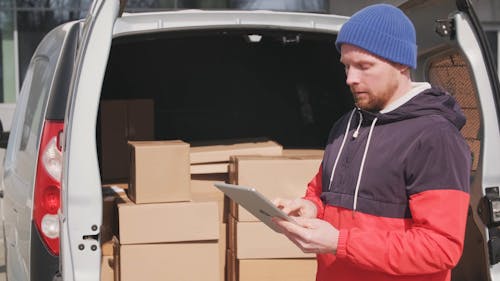 A Man Using An Ipad Standing At The Back Of A Delivery Van