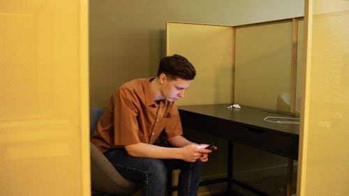 A Young Man Using His Cellphone While Seated Inside A Cubicle