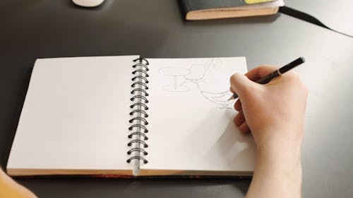 An Artist Drawing Furniture Designs On A Notebook