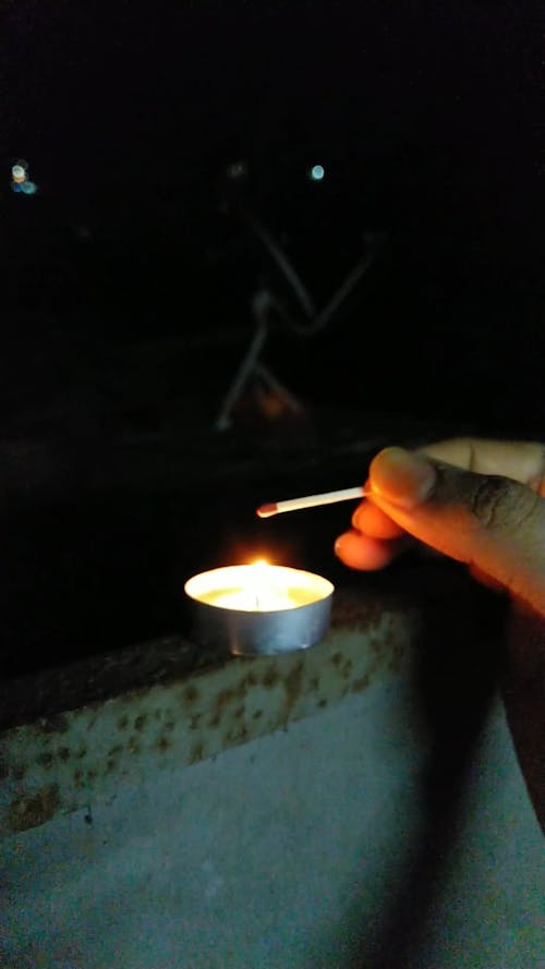 A Person Lighting a Match Stick from a Tealight Candle