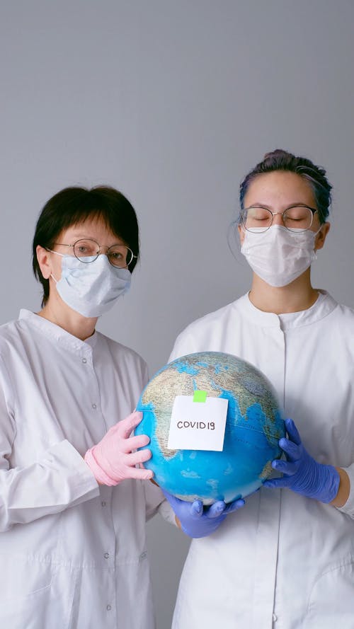 People With Face Masks and Latex Gloves Holding a Globe