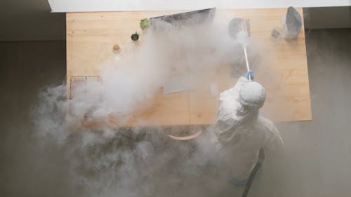 A Person In Protective Gear Disinfecting An Office With Steam