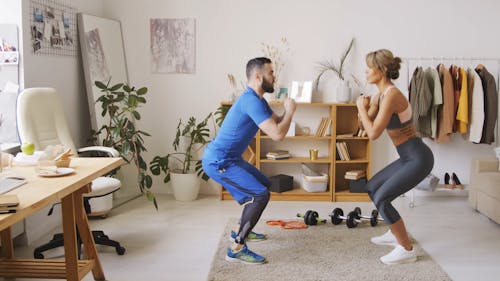 A Couple Squat Exercising At Home