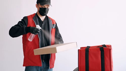 Delivery Man With Face Mask Disinfecting a Box