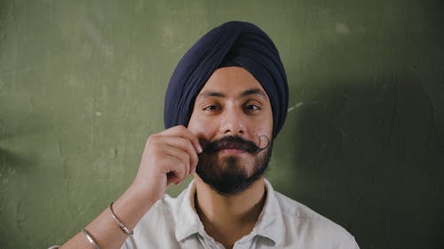 A Man Wearing A Turban Holding His Curly Moustache