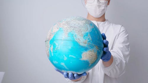 Person With Face Mask and Latex Gloves Holding a Globe