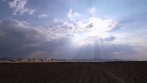 Driving On A Desert With Rays Of Sunlight Peeking Through The Clouds