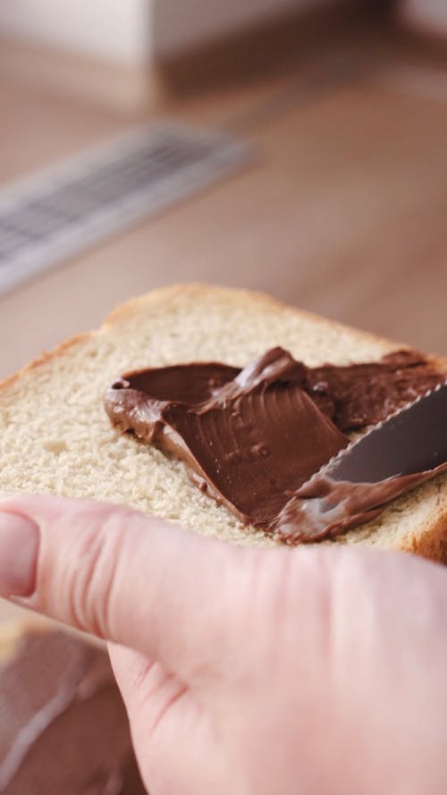 A Person Spreading Chocolate onto a Bread