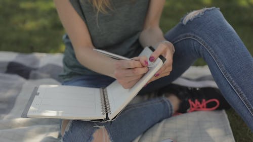 A Woman Writing Reminders On Her Planner Notebook