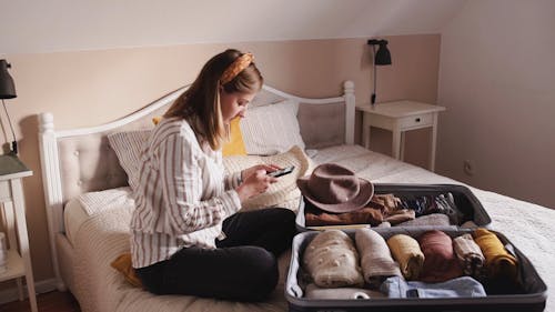 A Woman Uses Her Cellphone After Packing A suitcase