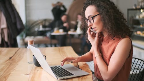 A Woman Working On Her Laptop While Talking On The Phone