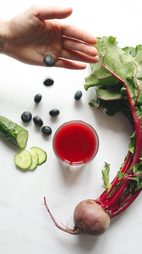 A Person Putting Berries by the Side of a Glass of Fruit Juice