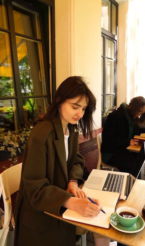 Woman Drinking Coffee and Writing on Her Notebook