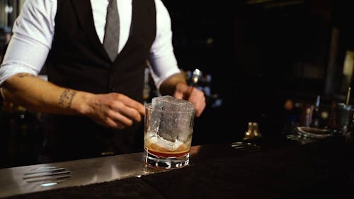 A Bartender Stirring an Ice Cube in a Glass