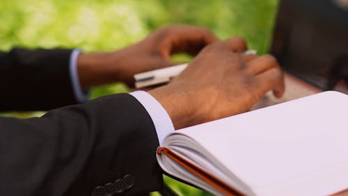 A Man Typing On A Laptop And Taking Notes