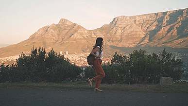 a woman walking down a road with mountains in the background