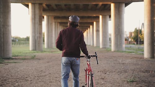 A Man Walking Under the Bridge while Carrying His Bike