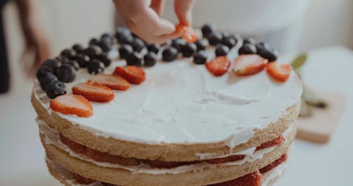 Person Decorating A Cake With Berries