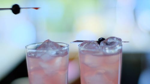 Close-Up View of Person's Hand Putting a Black Cherry on Iced Drinks