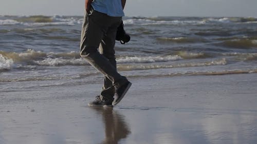 Person Walking on a Beach while Holding a Camera