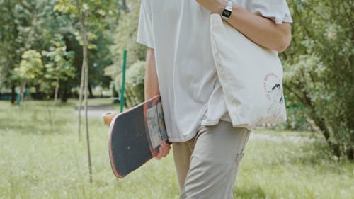 A Man Walking While Carrying a Skateboard 