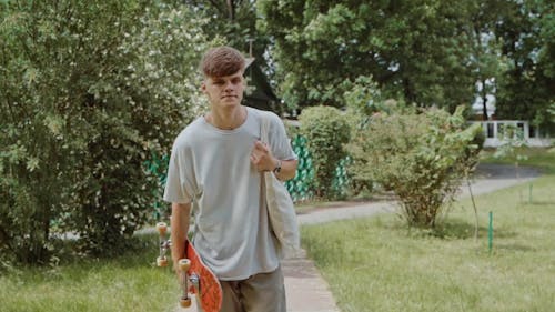 A Young Man Carrying a Tote bag and a Skateboard