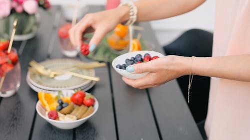 A Woman Putting Fresh Fruits On A Bowl