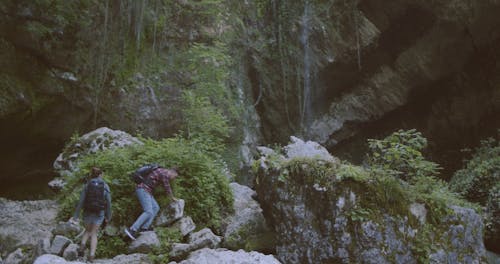 A Couple Hiking On Rocks Towards The Waterfalls