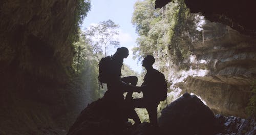 A Couple Resting On Cave Rocks Behind The Waterfall