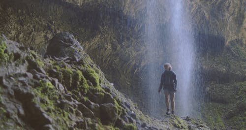 A Female Hiker Waling On A Trail Behind The Waterfall