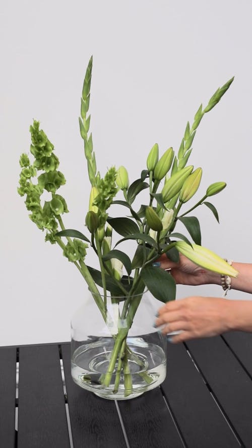 A Person Arranging The Plants In A Glass Vase